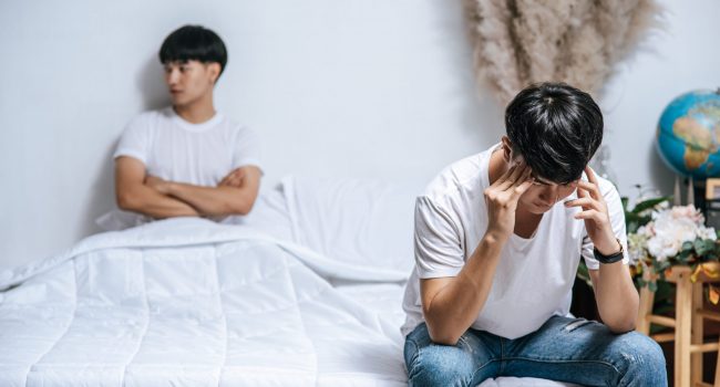 Two young men were angry on the bed and the other sat at the edge of the bed and was stressed.